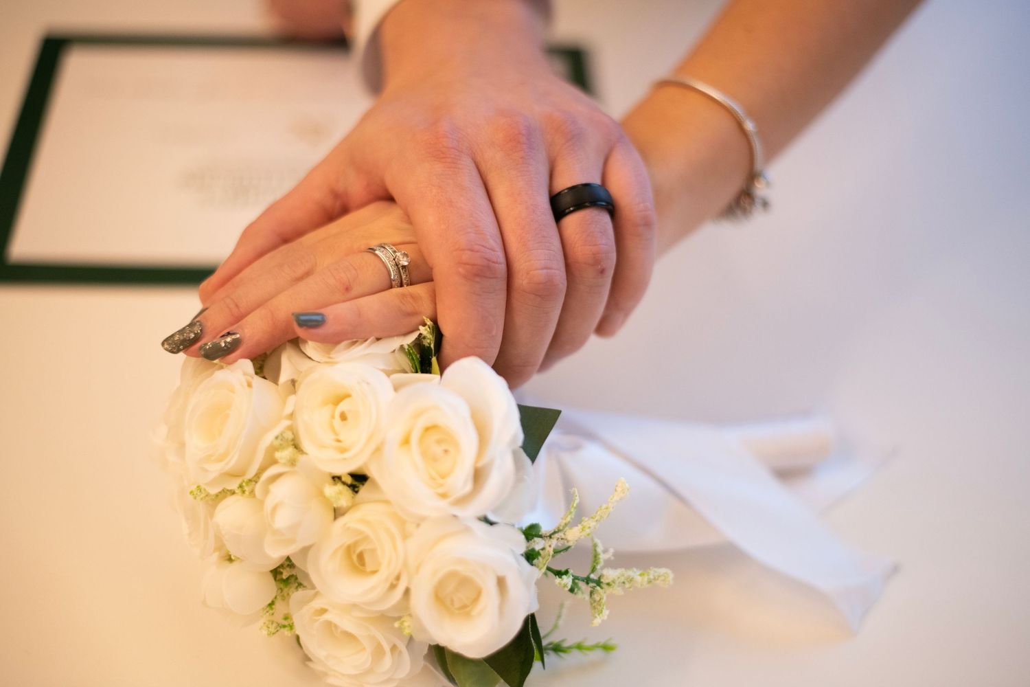 A bride in a white beaded wedding dress holding a red and white rose bouquet smiles during her wedding celebration.