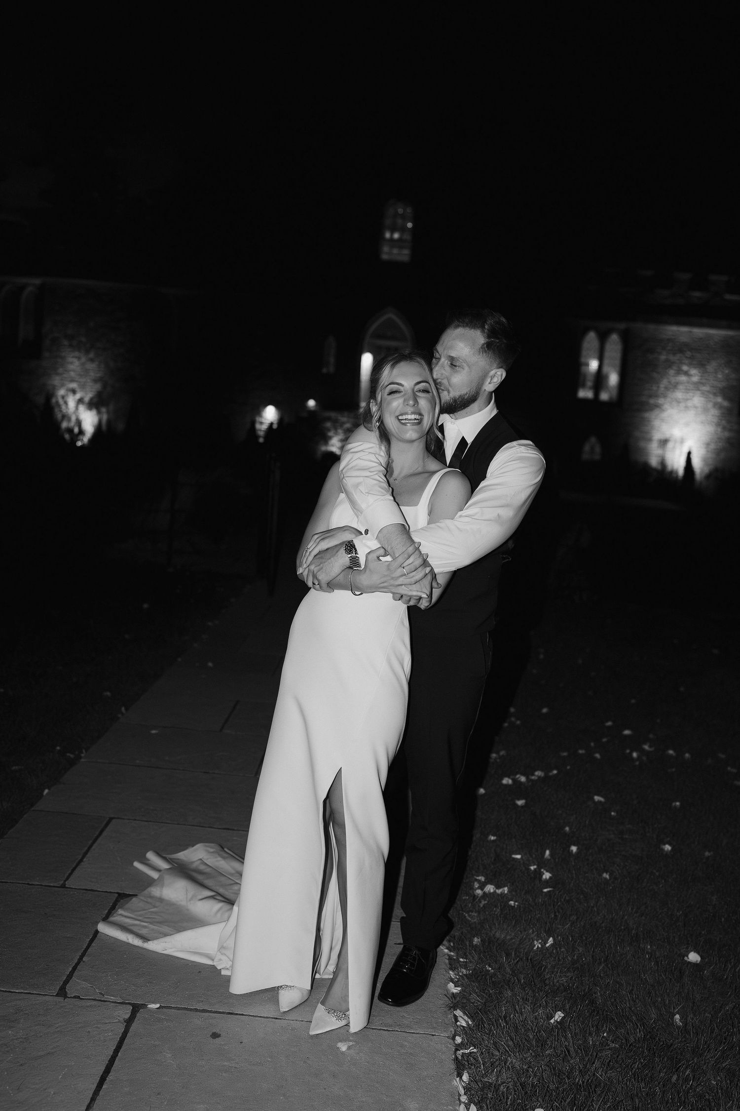 groom hugging bride from behind while kissing her cheek as she laughs at ivy lodge wedding in cirencester