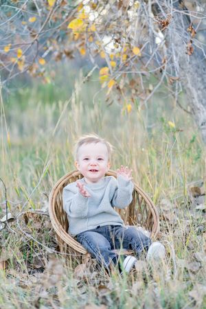 A set of three photos showing a small child sitting in autumn grass near a tree trunk wearing a gray sweater.