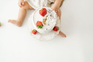 A white plate with fresh strawberries and whipped cream being served on a light surface.