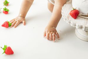 A close-up series of baby hands reaching for and touching fresh red strawberries on a white surface.