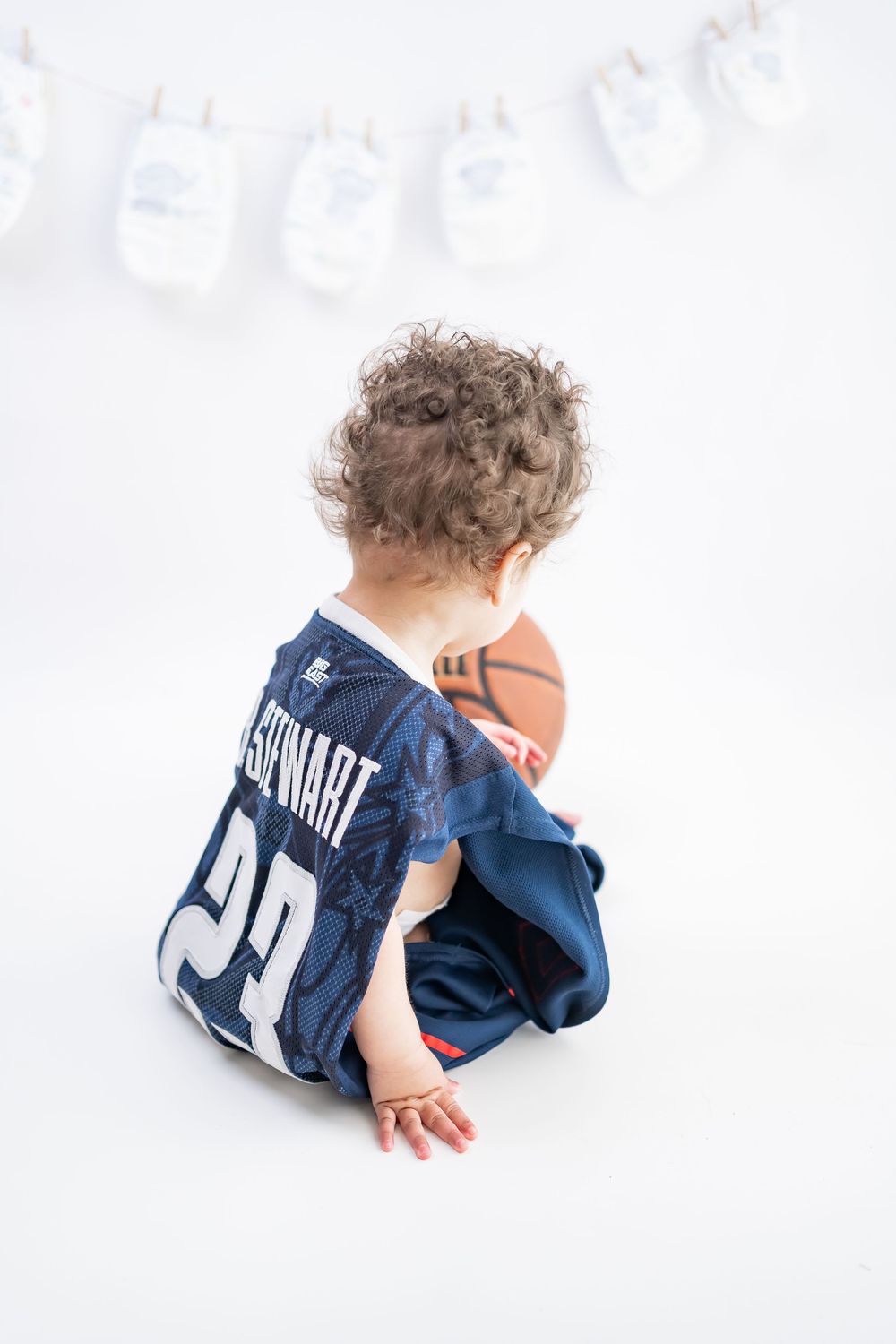 A series of photos showing a small child in a navy blue sports jersey crawling and playing on a white background.