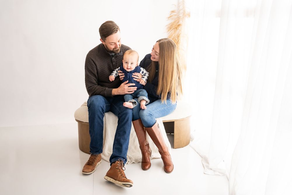 Parents and baby sitting together in a bright white studio during a family photography session.