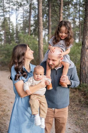 A family shares playful moments together in a pine forest setting while wearing coordinated blue and brown outfits.