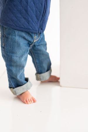 Close-up view of small bare feet peeking out from rolled-up blue denim jeans against a white background.