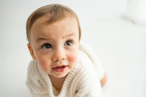 A small child in a cozy white sweater smiles while lying on a light background.