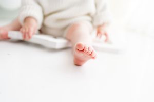 Baby's tiny feet peek out from soft white bedding while being gently held by adult hands.