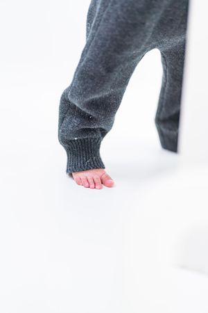 Bare feet with painted pink toenails peeking out from dark gray sweatpants against a white background.
