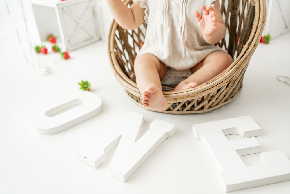 Small feet resting in wicker basket next to white decorative letters on white surface.