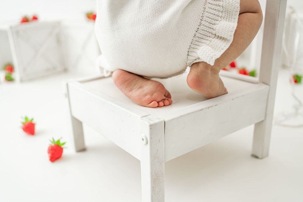 Tiny feet peek out from white fabric against a bright, airy background with scattered strawberries.