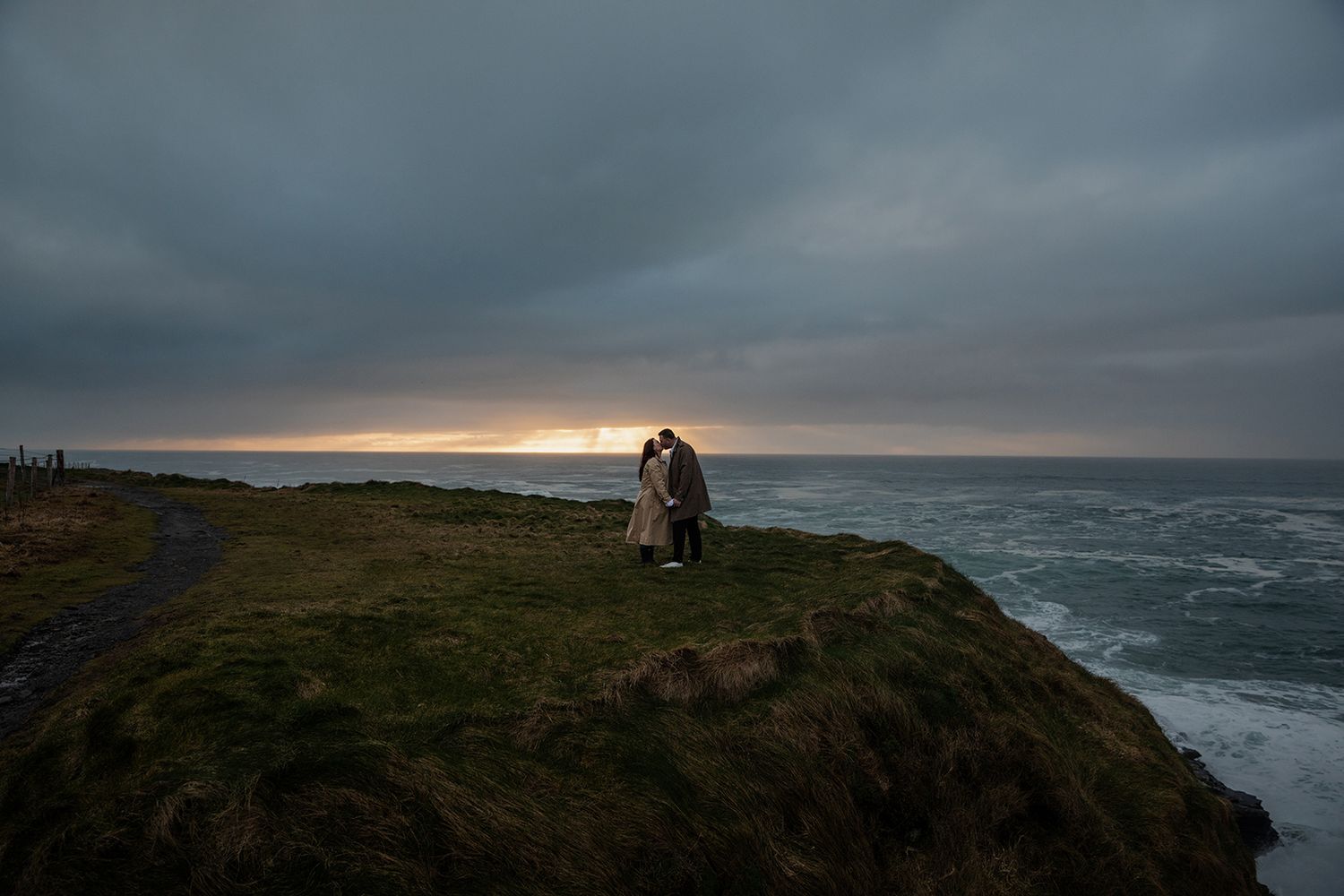 Couple standing on Cliffs of Moher during stormy coastal engagement session at golden hour