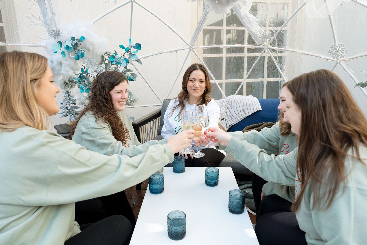 Bride surrounded by bridesmaids wearing matching sweatshirts — candid wedding celebration portrait