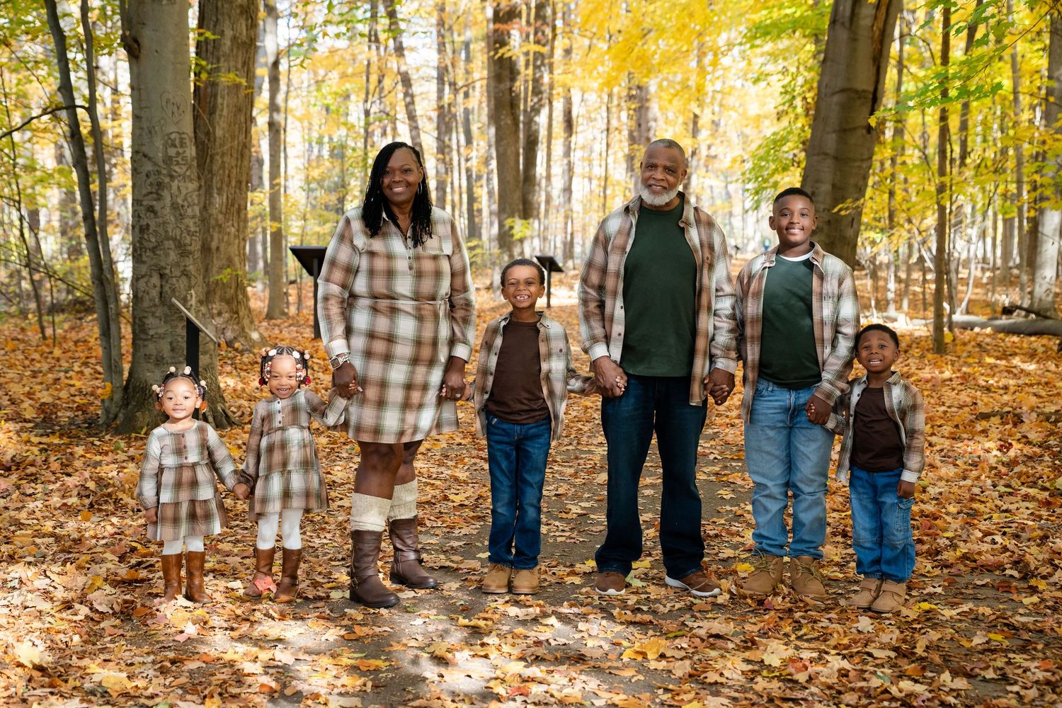 Family walking through autumn forest with golden leaves and tall trees in panoramic view.