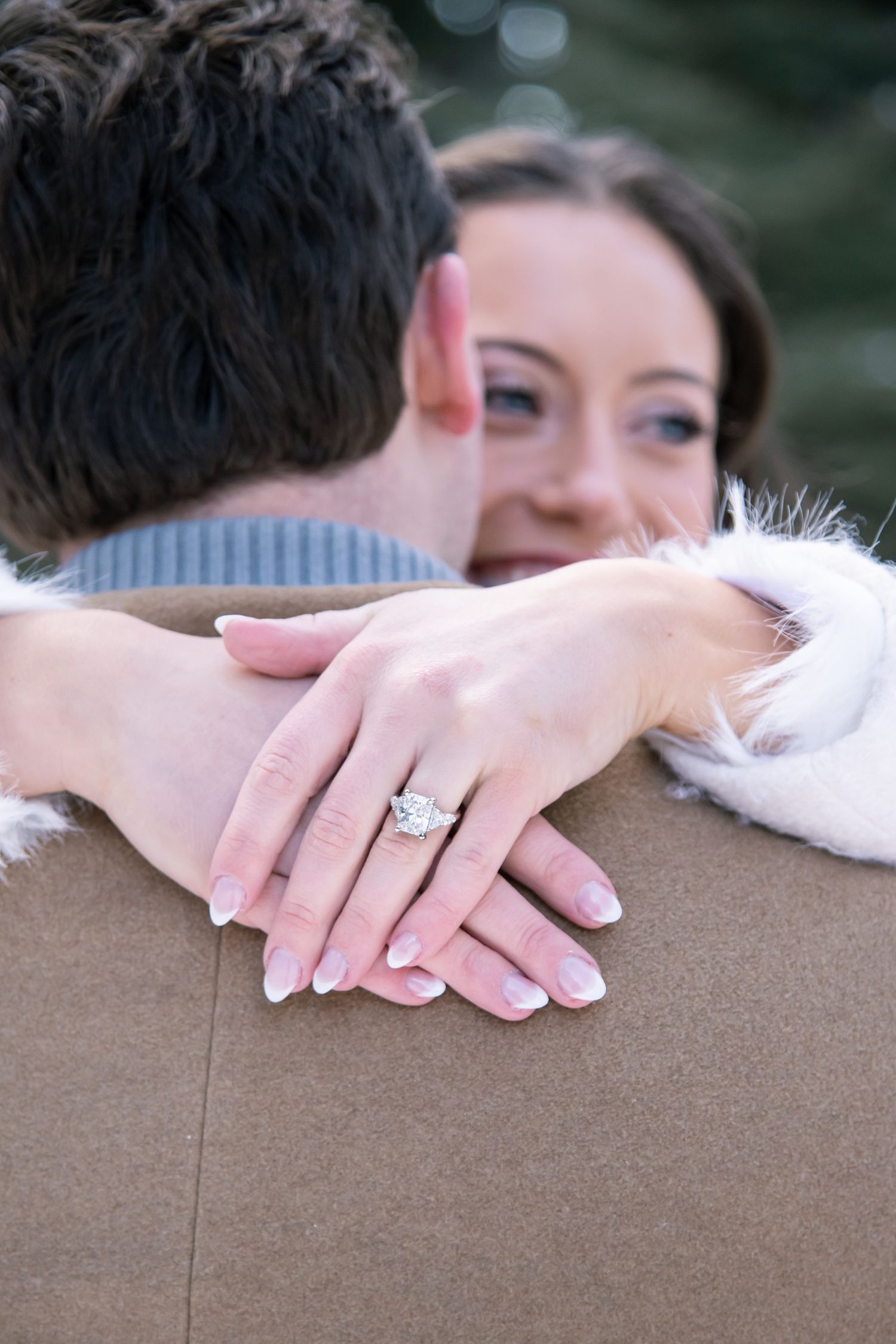 A couple embraces in a romantic moment outdoors with hands visible against a blurred natural background with Vail engagement photographer