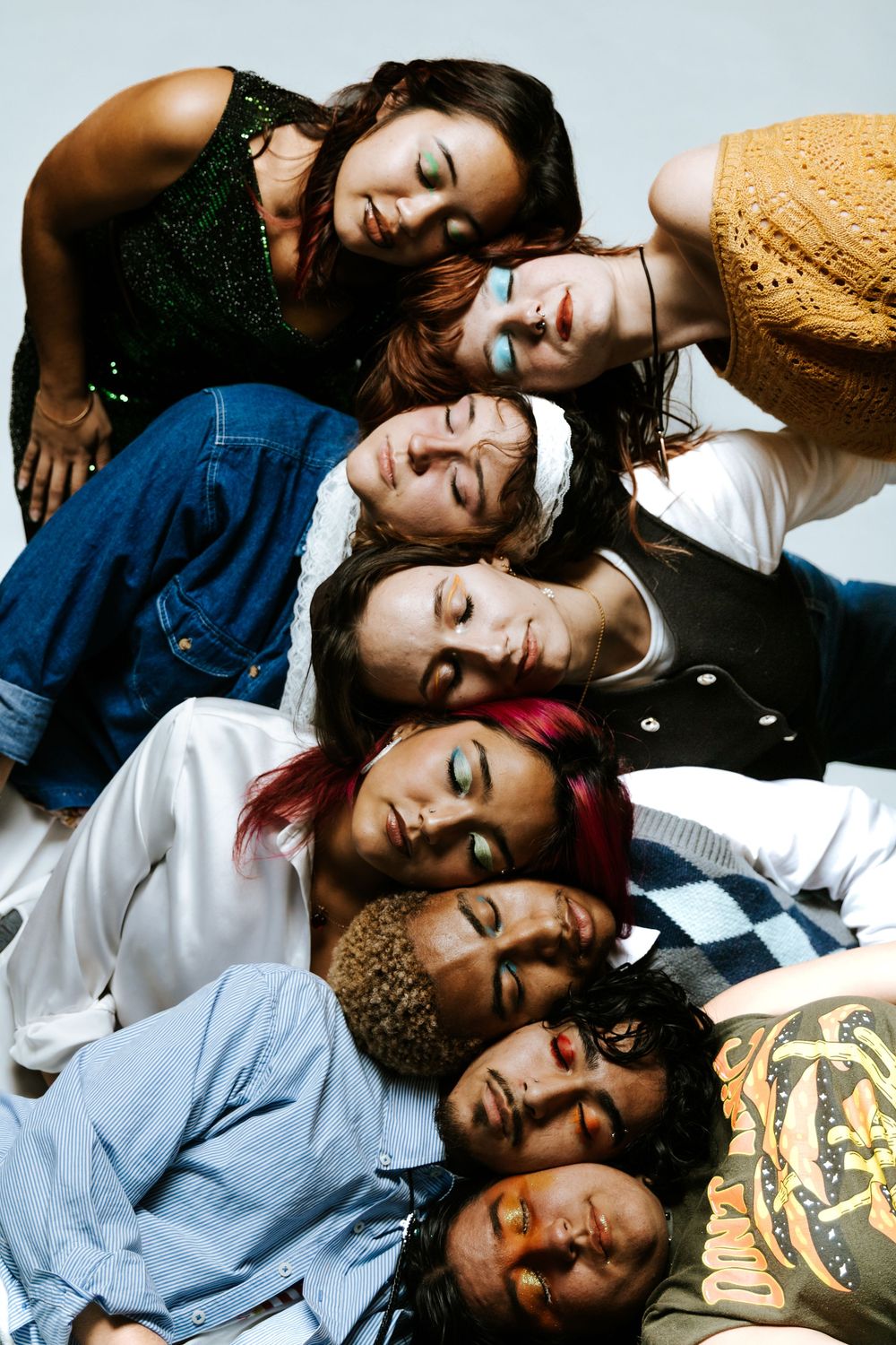 Seven diverse young people lying together with heads touching, eyes closed, in a creative group portrait.
