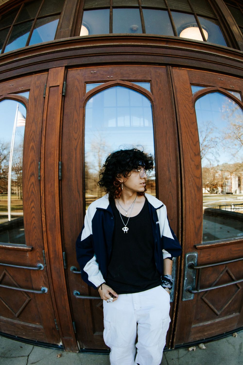 Figure in black and white outfit posing against wooden doors with arched windows.