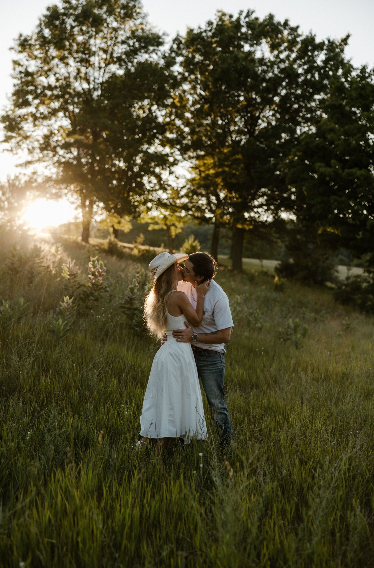 A couple embraces in a grassy field at sunset, with trees in the background. Fort Worth Texas wedding photographer.