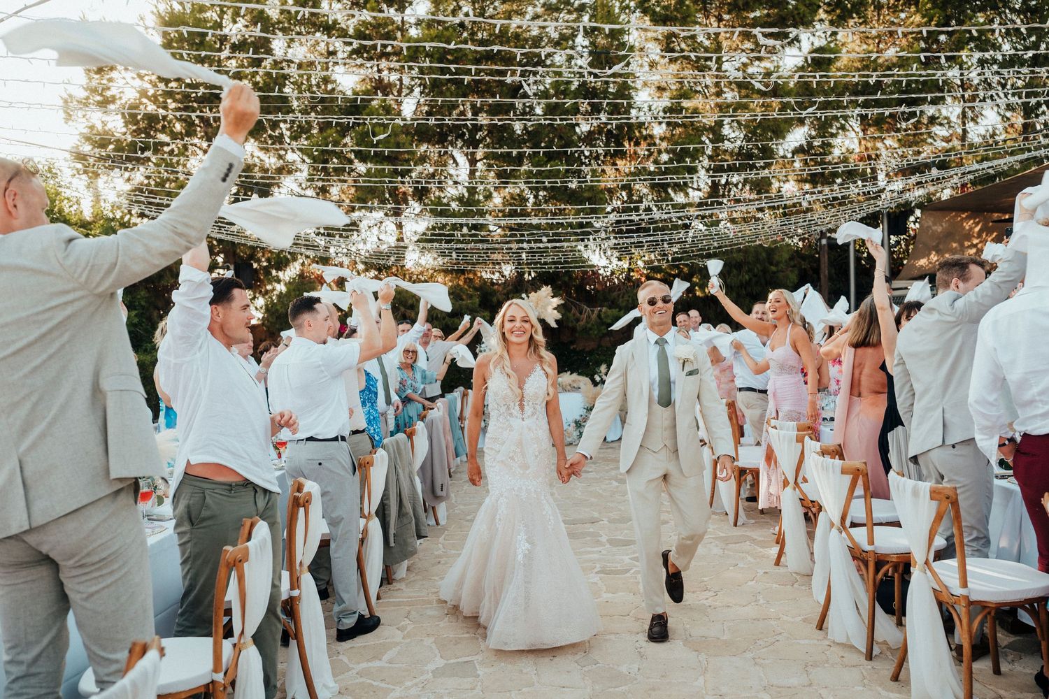 A couple dances joyfully on an oceanfront terrace with palm trees in the background.