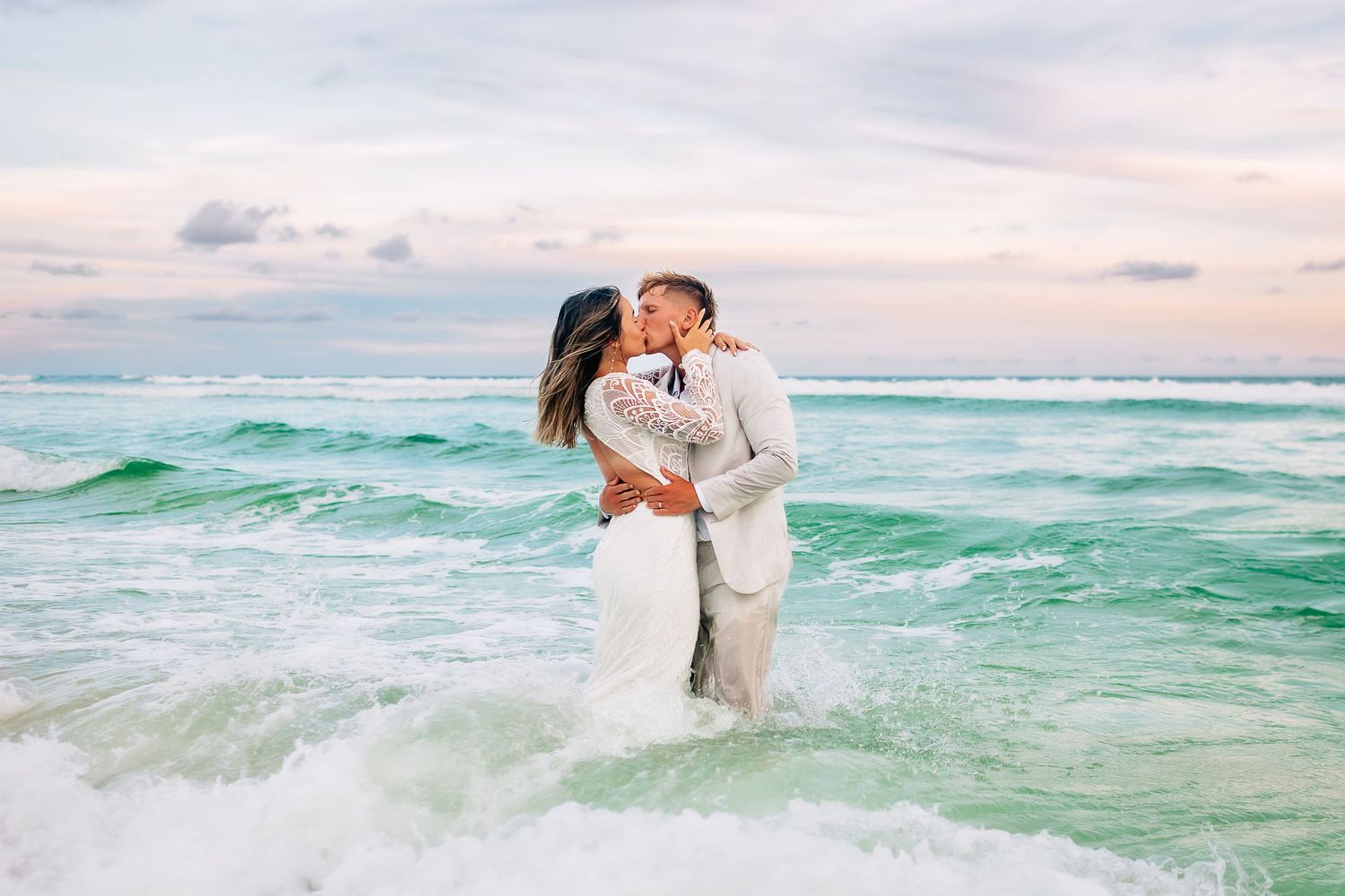 Couple embracing romantically on a sandy beach at sunset with turquoise ocean waves in the background.