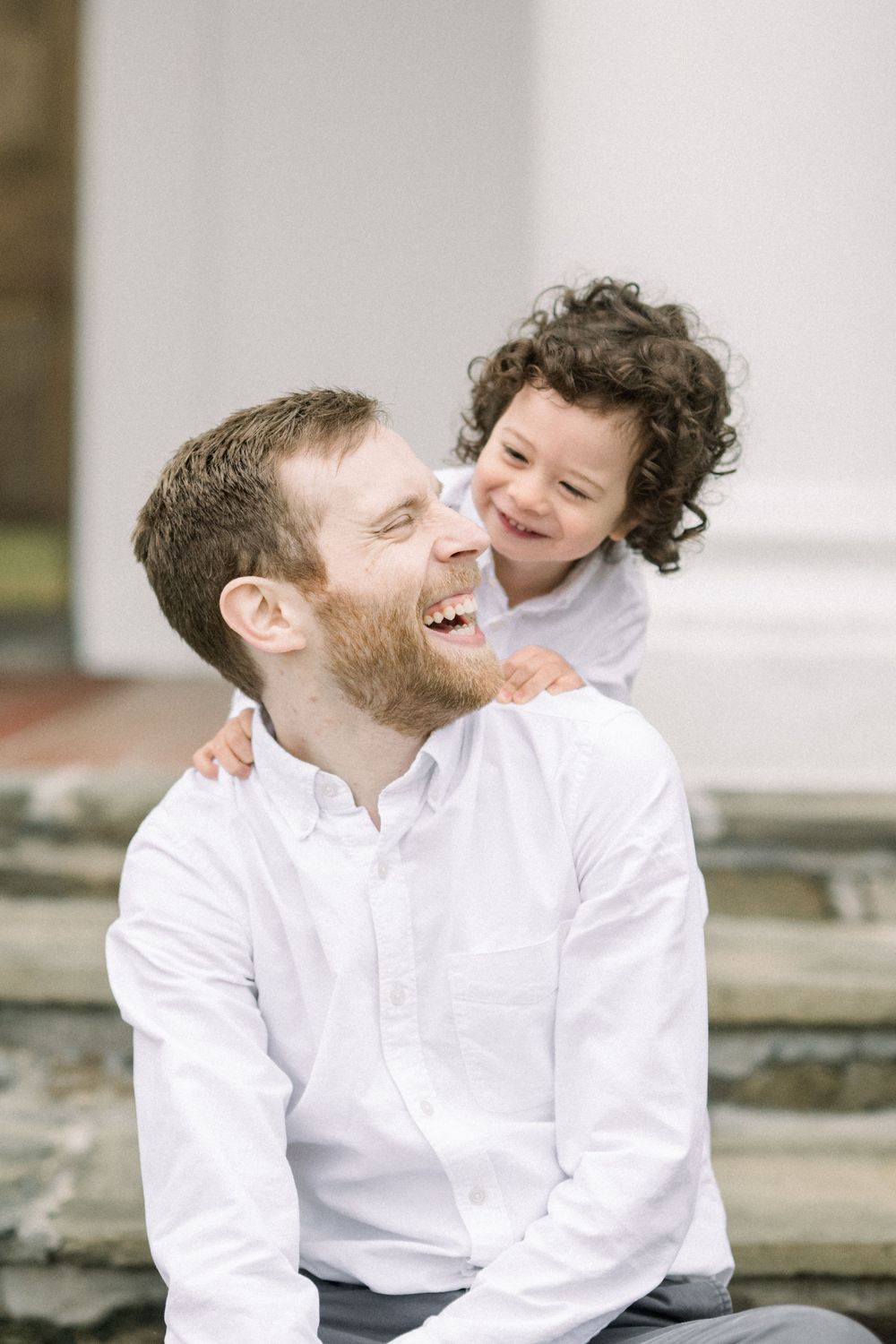 Two people in white button-down shirts share a candid laughing moment together outdoors.