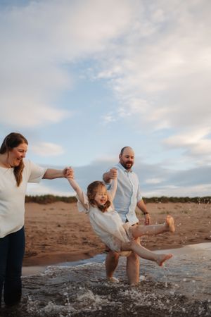 Family playing and splashing in shallow water at beach during golden hour.