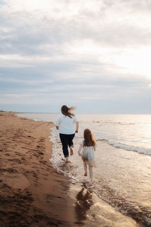 Two people running along beach shoreline at sunset while waves crash nearby.