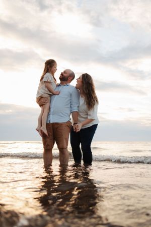 Family standing together in ocean waves during sunset at beach.