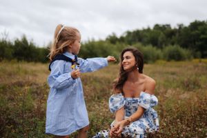 Family wearing coordinating blue and white outfits plays together in a golden field at sunset.