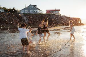Group enjoying sunset at the beach with houses visible in background while playing in shallow water.