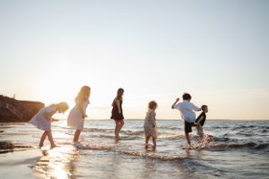Silhouettes of people playing and splashing in ocean water during sunset.