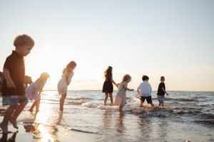 People wading and playing in ocean waves during sunset creating beautiful silhouettes.