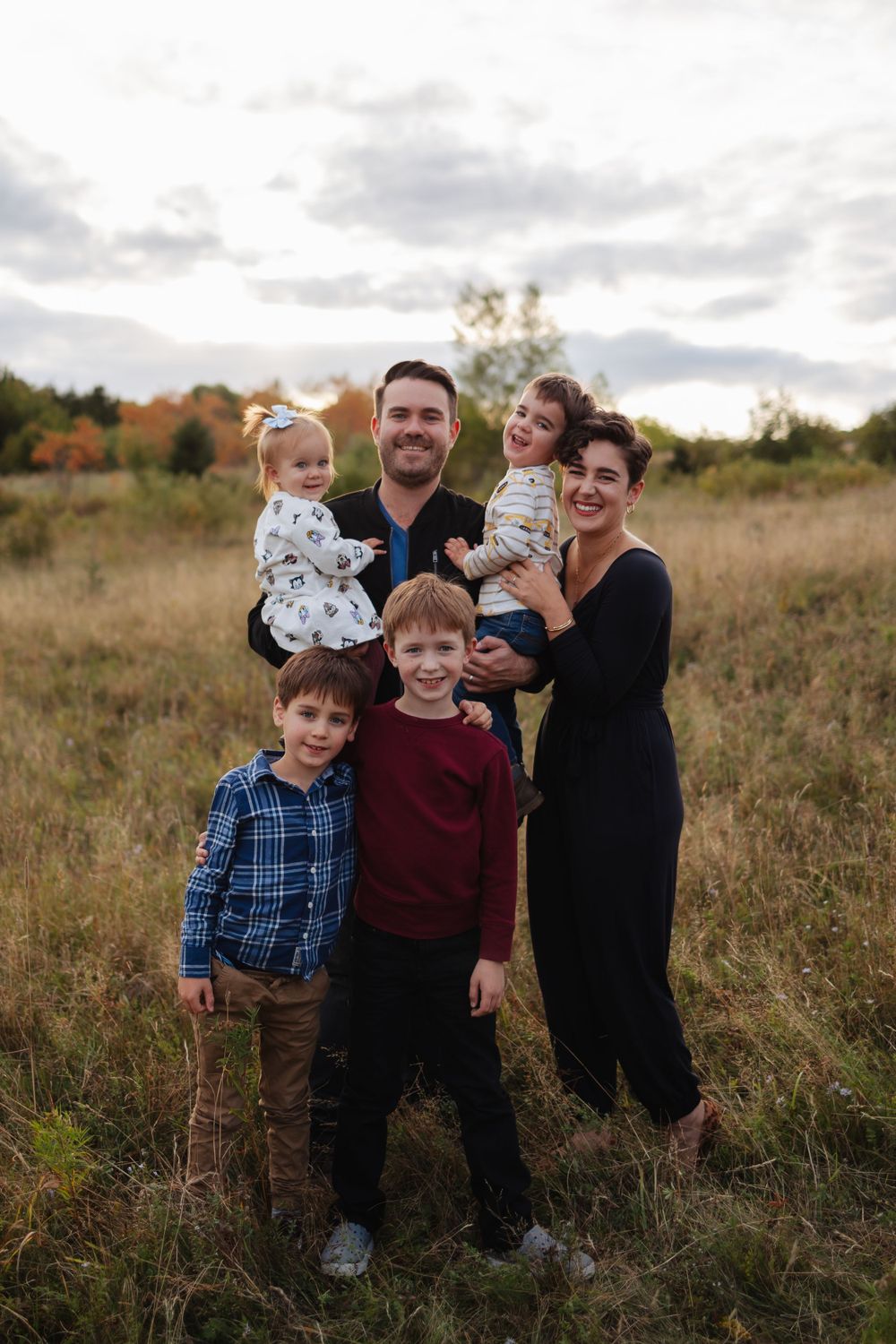 A group photo in a scenic autumn field with cloudy skies.
