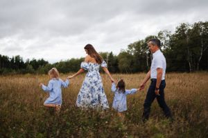 Family members walking and playing together through tall grass in a natural field setting.