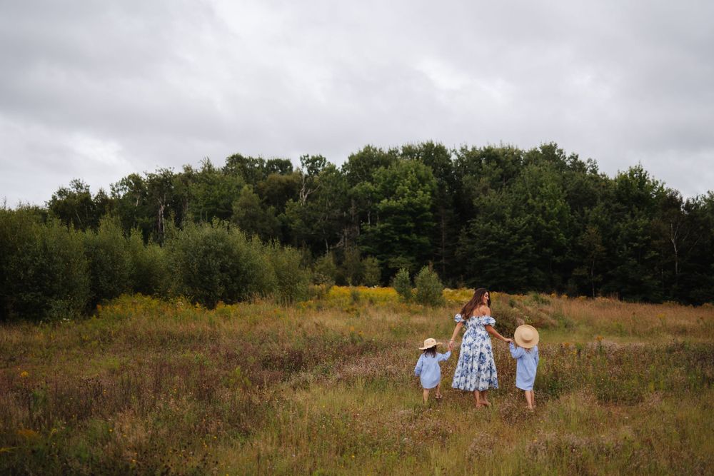 Panoramic view of a family photoshoot in a scenic meadow with trees in the background.