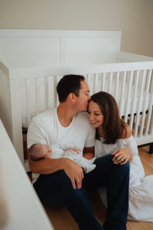Tender family moment in a nursery with white crib and soft natural lighting.