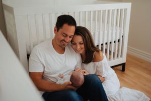 Intimate family portrait in nursery with white crib and hardwood floors.