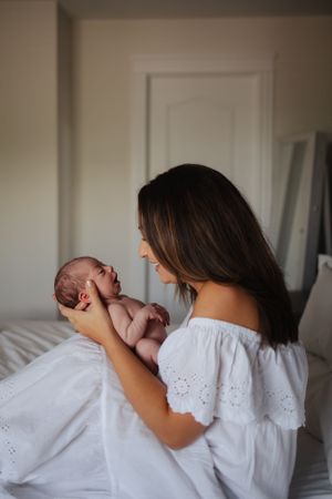 Mother in white dress sharing joyful moment with animated newborn baby.