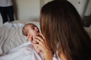 Intimate moment between mother and newborn baby on white bedding.