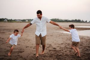 Family playing and running together on wet sand at beach during sunset.