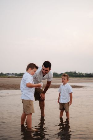 Parent and children standing in shallow ocean water during sunset.