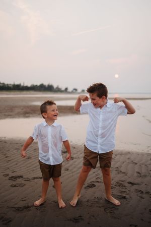 Children in white shirts playing and dancing on dark sandy beach at dusk.