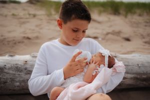 Family moment captured on sandy beach with driftwood and coastal grass.