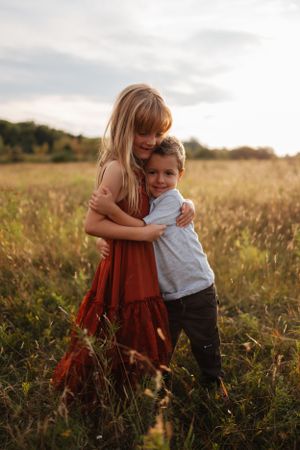 Two people sharing a sweet embrace in a rustic field during sunset.