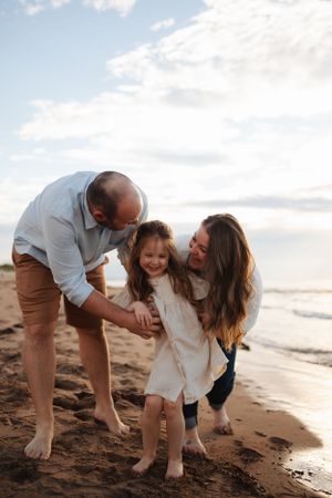 Family playing together on sandy beach at sunset with ocean in background.