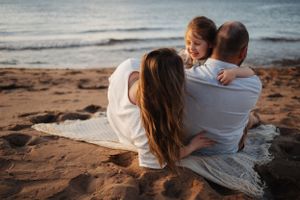 Family sitting together on beach blanket watching sunset over ocean.