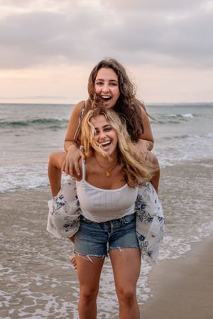 Two Sisters on piggyback laughing and having fun on a beach at sunset in Palos Verdes, California