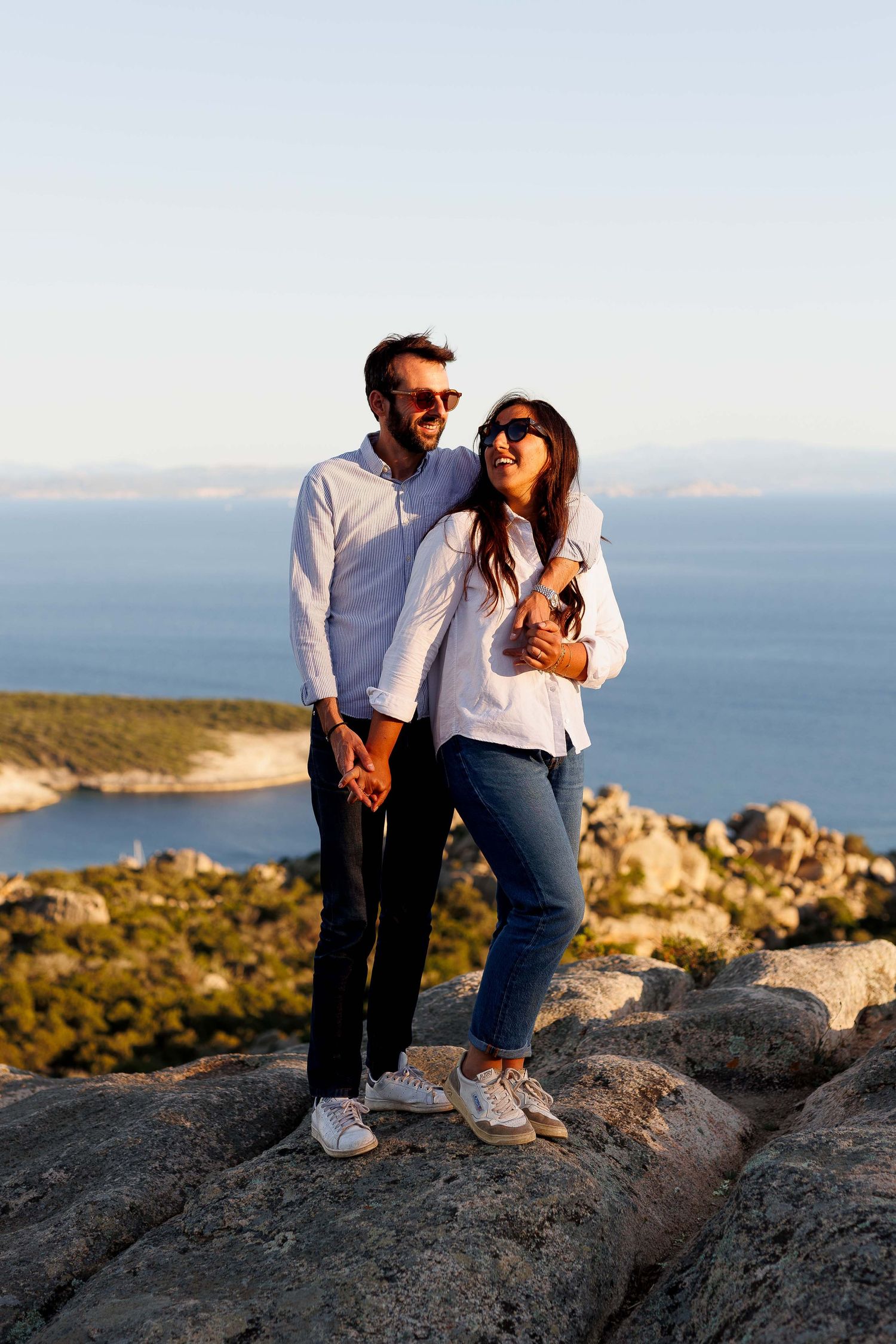 Couple kissing on rocky hilltop with scenic ocean and island views in the background during golden hour.
