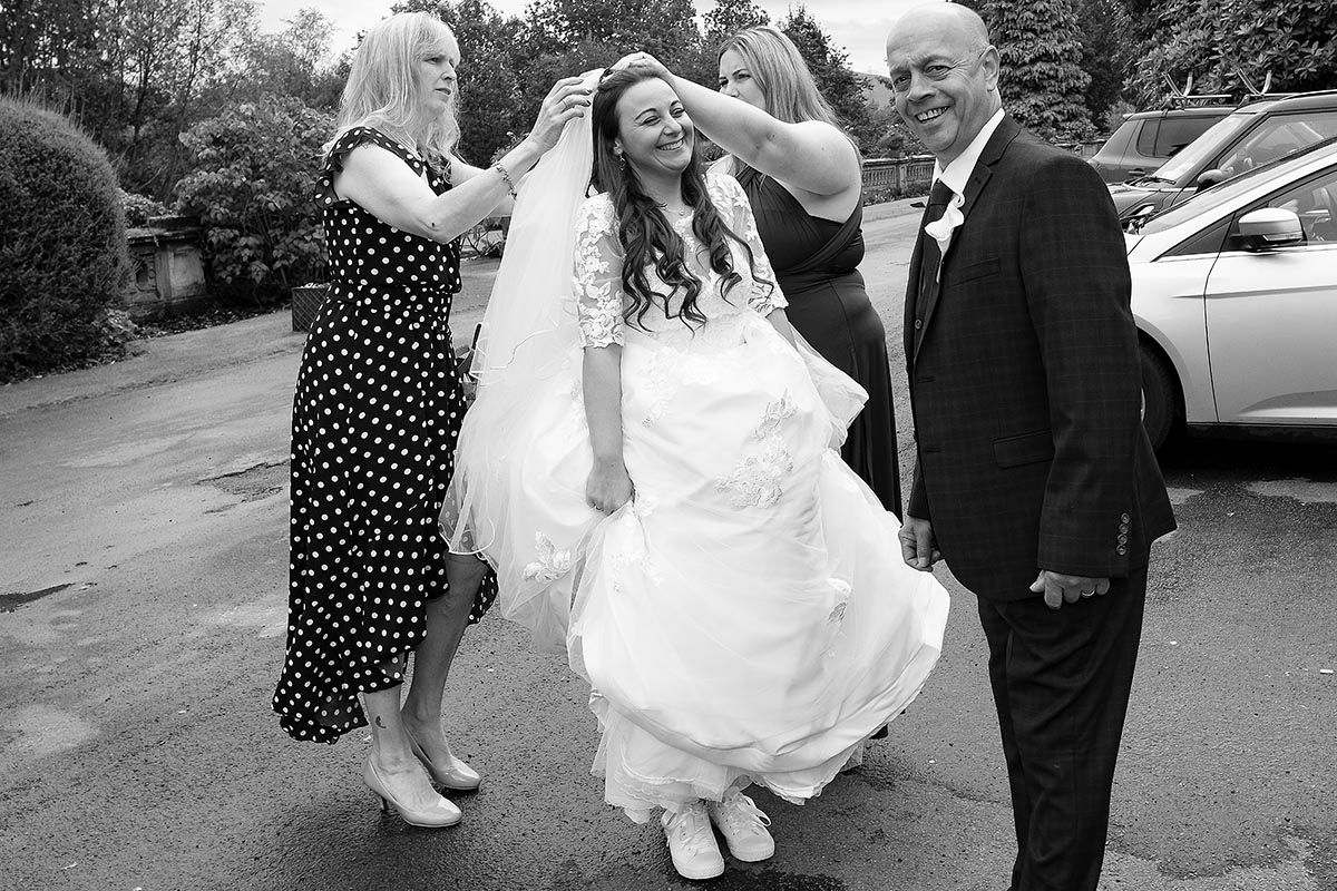 Black and white wedding photo of bride having her veil adjusted by two friends in front of Auchen Castle wedding venue