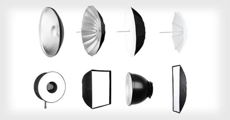 A collection of professional photography studio lighting modifiers including beauty dishes, softboxes, and umbrellas on white background.