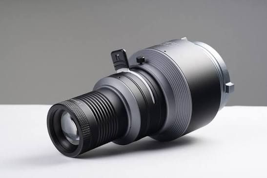 Black professional camera zoom lens lying on its side on a white surface against a gray background.